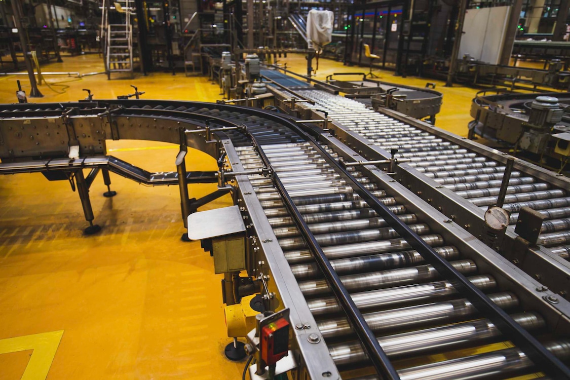 Two roller conveyors, with one taking a turn and the other transferring to a plastic belt